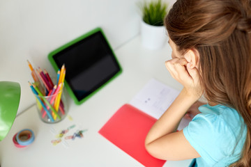 girl with tablet pc writing to notebook at home