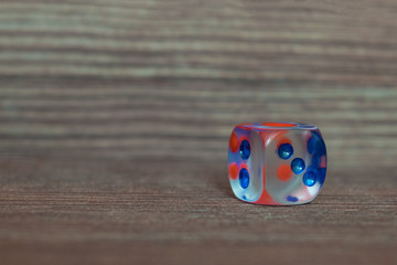 Single transparent dice on wooden board. Six sides with blue and red points.