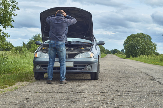 Worried Man Holding His Head By Hands Standing Near His Old Broken Car With Raised Hood On The Road       