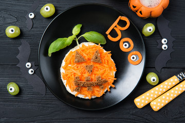 Funny toast with carrots in a shape of pumpkin and grapes monsters, sandwich for kids Halloween idea, top view on wooden background