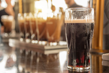 Close up of a glass of stout beer in a bar, irish pub, Saint Patrick day celebration - obrazy, fototapety, plakaty