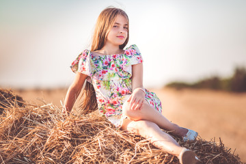 Pretty girl is sitting on stack of hay in the field