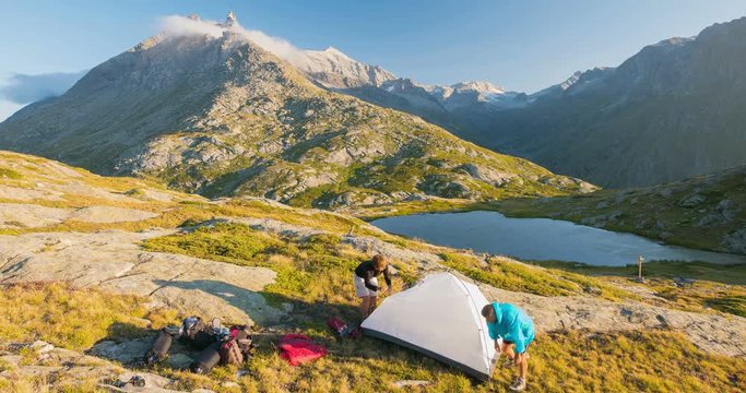 Couple of people setting up a camping tent on the mountains, time lapse. Adventures on the Alps, majestic peak and alpine lake in the background.