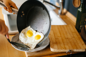 Two fried eggs in a pan with olive oil. Girl's hand holding a frying pan with scrambled eggs.