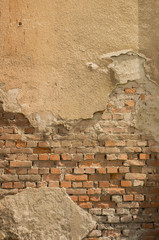 Aged yellow wall with bricks and broken plaster