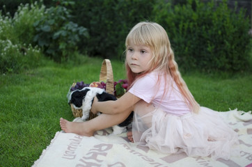 Little blond girl sitting on the cover with her pet - black and white puppy shih tzu.