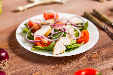 Fresh salad with chicken, tomato and greens on wooden background top view. Healthy food.
