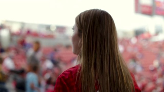 Closeup Of Female Sports Fan Walking, With Back To Camera, Around Professional Stadium On Game Day (Jumbotron In Background)