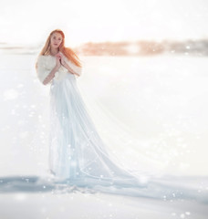 Fototapeta na wymiar Snow fairy, the snow Queen. Girl in a white dress standing in the snow, wonderful way. Christmas fairy