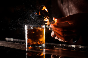 The bartender makes flame above cocktail