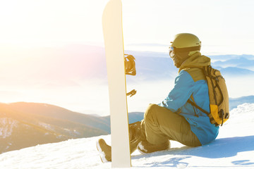 Male snowboarder sitting at the very top of a mountain and taking a look at landscape