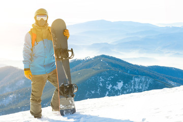 Young snowboarder standing next to snowboard thrusted into snow with beautiful scenery on background