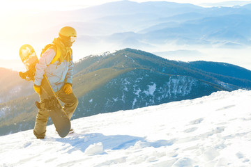 Young snowboarder in helmet walking at the top of a mountain