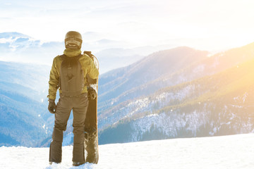 Fototapeta na wymiar Young snowboarder standing next to snowboard thrusted into snow and looking at a beautiful mountain scenery