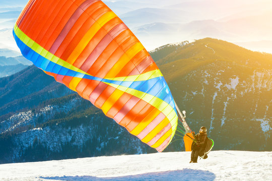 Paraglider launching into air from the very top of a snowy mountain slope