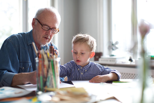 grandfather helping grandson with homework. concentration, kindergarten teacher, glasses, study.