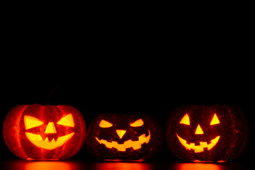 Three spooky carved pumpkins on table in darkness