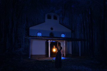Beautiful girl in long dress with lantern alone in the dark forest