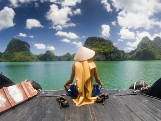 man wearing a Vietnamese hat enjoying the magnifiecent sight of Ha Long bay limestone rocks on a...