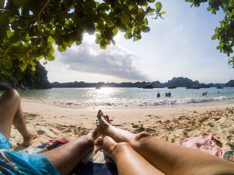 legs of couple relaxing on a sandy tropical beach - holiday concept