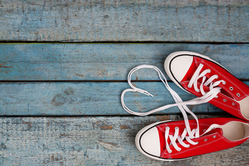 A pair of red retro sneakers on a blue wooden background, laces lined in a heart shape. Concept of...