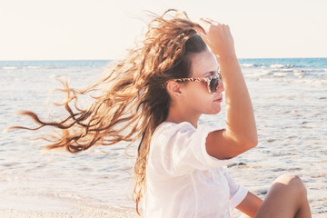 A young woman in sunglasses holds a hand to her hair fluttering