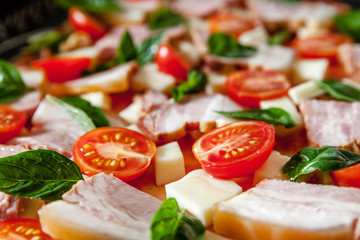 Raw Italian pizza from cherry tomato, basil, mozzarella cheese and bacon ham ready for baking, close-up.