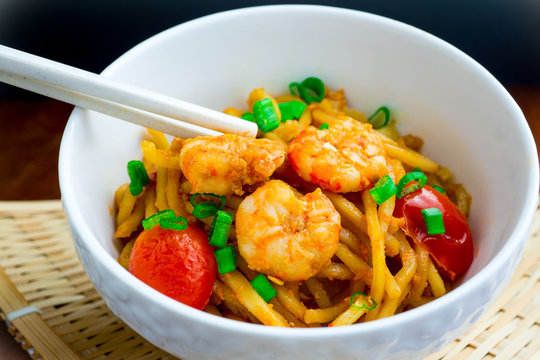 Fried yellow noodle with prawn pinch chopsticks on table