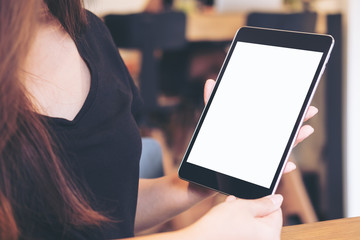 Mockup image of a beautiful Asian business woman holding and looking at black tablet pc with blank white screen in modern cafe