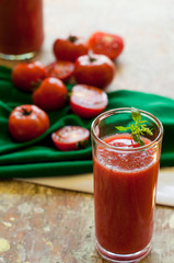 Glass and bottle of tomato juice with vegetables and green napkin on wooden background