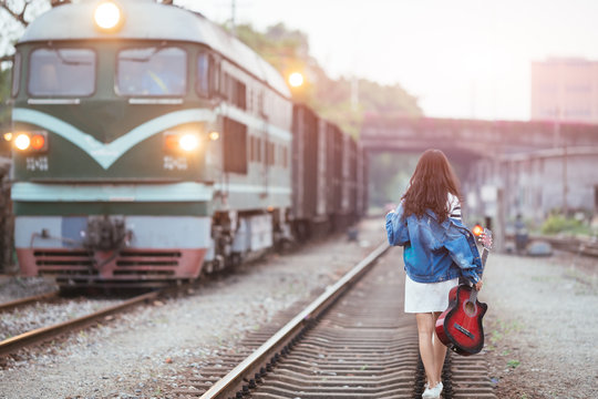 Beautiful girl with guitar walking on railway tracks at railway station
