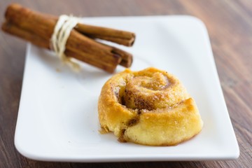 Single cinnamon roll served on white rectangle plate and decorated by a pack of cinnamon sticks
