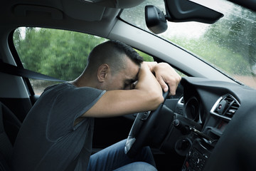 young man resting on the steering wheel of a car