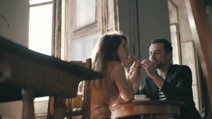 Man in love holding a beautiful young woman by hand at the table at a loft cafe