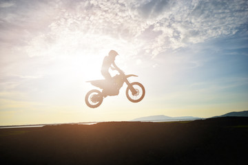 Fototapeta na wymiar The silhouette of a motorcycle motocross jump from the hill at sunset.