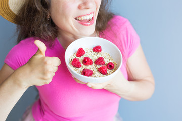 Smiling woman hold healthy and natural breakfast, oatmeal and raspberries in a bowl