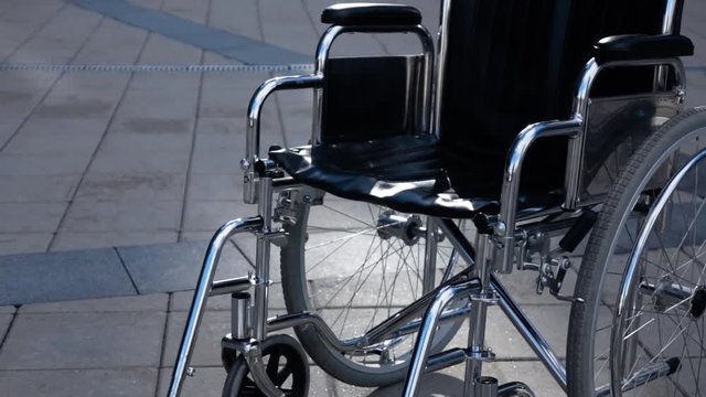 Invalid wheelchair rolling near modern building. Sunny teal and orange steadicam shot. Imminent illness concept. Disease.