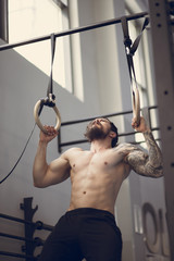 Fitness handsome man doing dipping exercise using rings in the gym