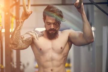 Young fit man pulling up on gymnastic rings.