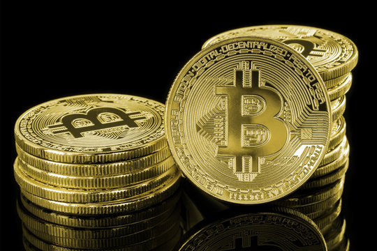 Single golden Bitcoin in front of two stacks of golden coins isolated on a reflective, black background. Conceptual image to visualize cryptocurrency.