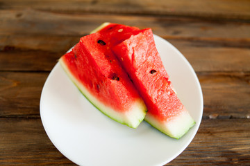 Ripe red watermelon on a wooden background. Slice of watermelon berries in a white plate