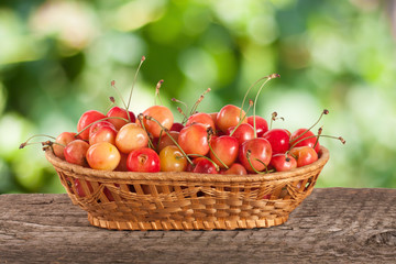 Yellow cherry in a wicker basket on a wooden table with a blurry garden background