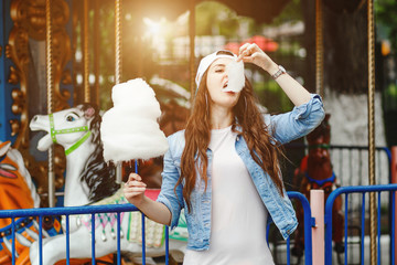 Young woman in stylish denim clothing eating Cotton candy in amusement park