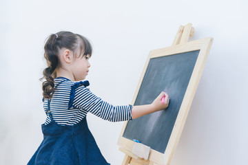 A little cute girl enjoy drawing on blackboard by chalk, education by herself