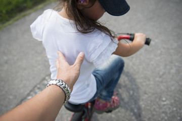 Hand pushing the back of a child riding a bicycle