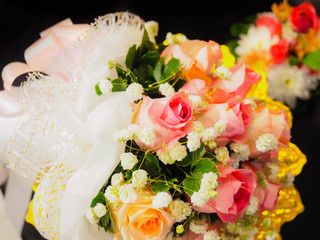 pink and orange rose with white small flower put on asia style pedestal with soft focus flower and black background
