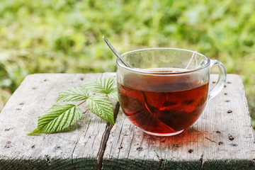 Glass cup of tea with metal spoon in it on a wooden rustic board and green grass on the background