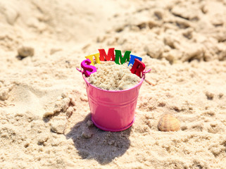 Fototapeta na wymiar Pink baby bucket with sand and inscription summer