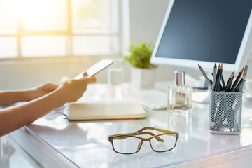Close-up of female hands using smart phone while working on computer at modern office interior