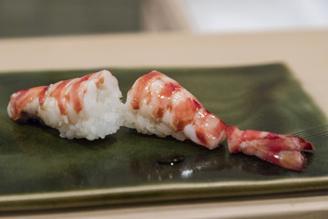 Shrimp tail nigiri sushi with white rice on green plate closeup